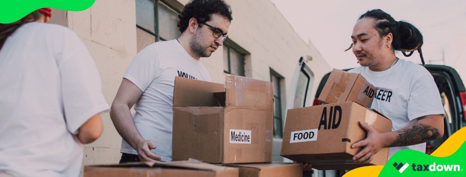 Dos personas voluntarias llevan cajas de cartón con medicinas y comida
